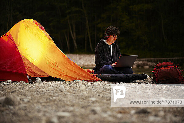 Young businesswoman using laptop sitting by tent