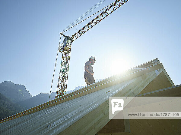 Carpenter standing on roof at construction site under clear sky