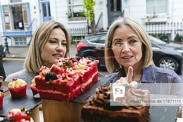 Senior woman choosing pastry with daughter seen through store window