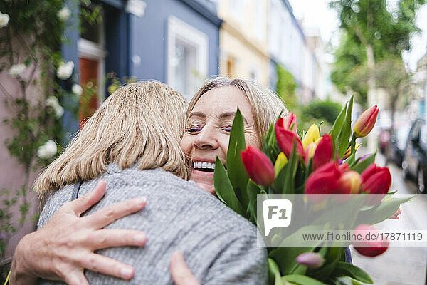 Glückliche ältere Frau mit Blumen  die ihre Tochter umarmt