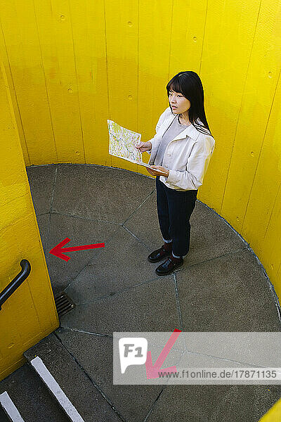 Confused woman holding map standing in front of wall