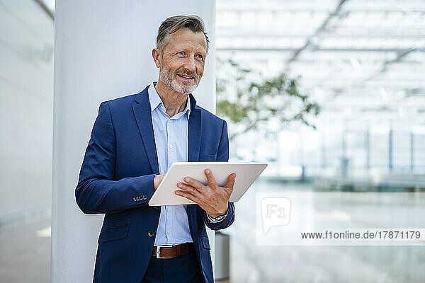 Smiling businessman holding digital tablet in front of column