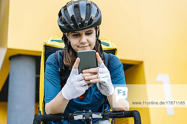 Smiling delivery woman wearing helmet text messaging through smart phone