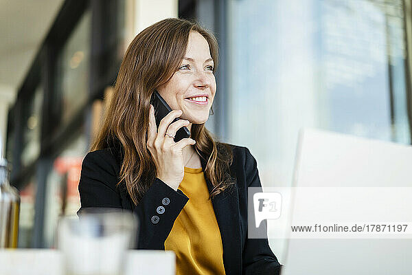 Smiling businesswoman talking on smart phone at cafe