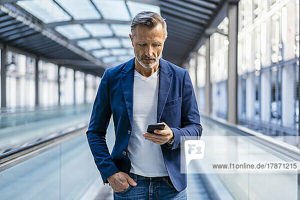 Businessman with hand in pocket using smart phone on escalator