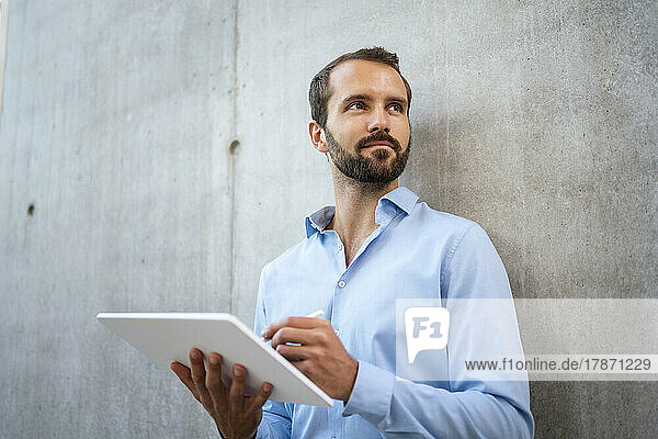 Smiling young businessman with tablet PC standing in front of wall