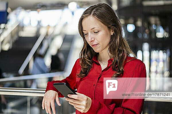 Woman with brown hair using smart phone leaning on railing