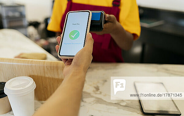 Hand des Kunden  der im Café kontaktlos per Smartphone bezahlt