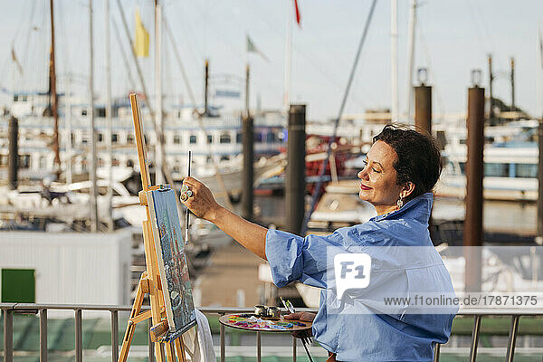 Female painter measuring by easel at harbor