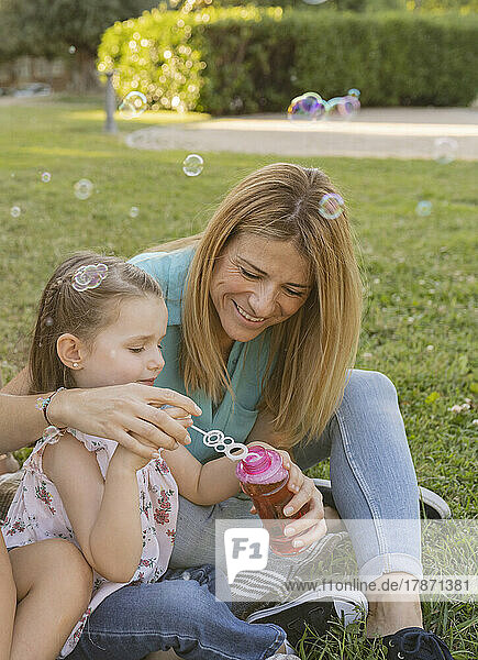 Lächelnde Frau mit Tochter  die einen Seifenblasenstab in eine Flasche taucht