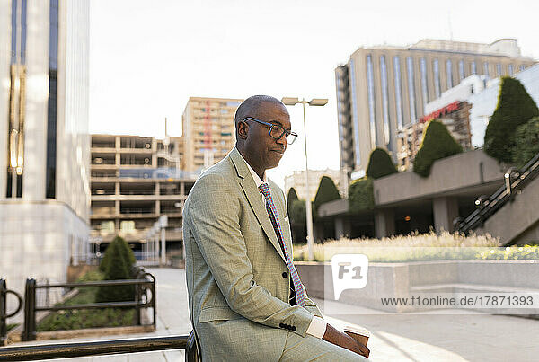 Thoughtful businessman with coffee cup sitting on railing