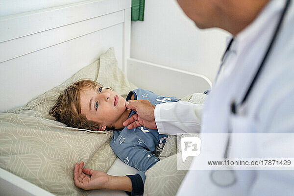 Doctor examining boy in bed at home