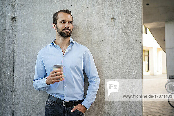 Junger Geschäftsmann mit Kaffeetasse steht vor der Wand