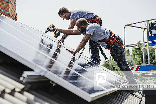 Craftsmen installing solar panels on house rooftop