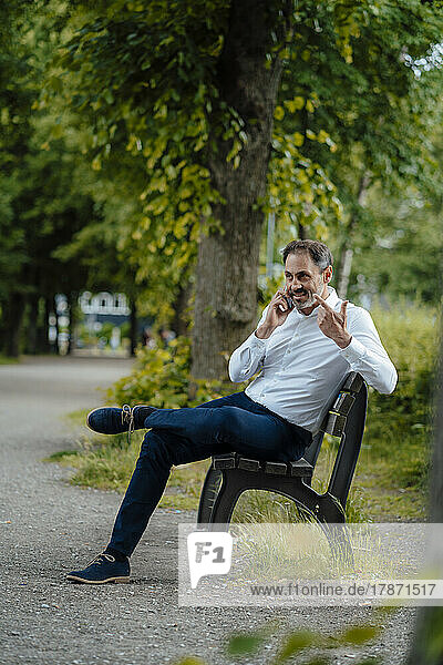 Businessman talking through mobile phone sitting on bench at park