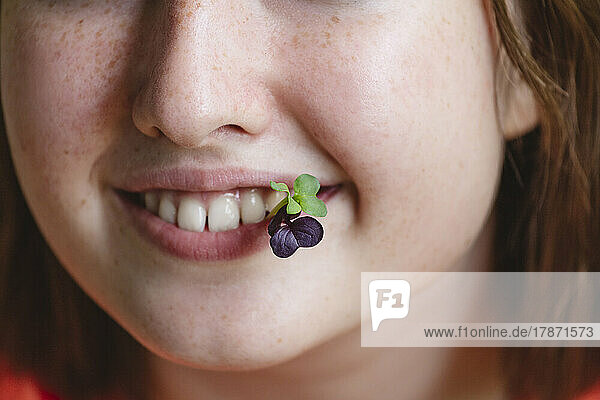 Smiling girl with fresh microgreens in mouth