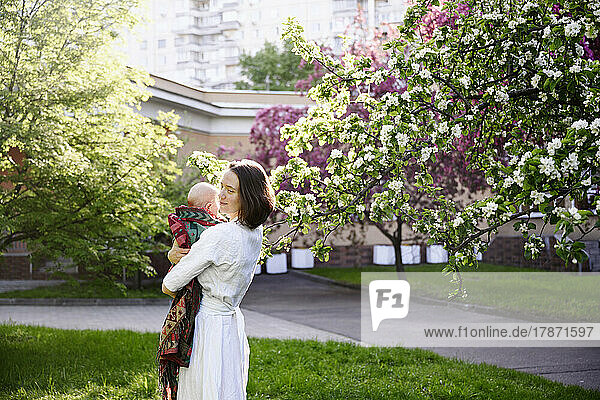 Smiling woman with baby standing in apple blossom garden
