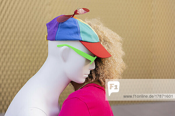 Young woman hugging woman wearing multi colored cap in front of wall
