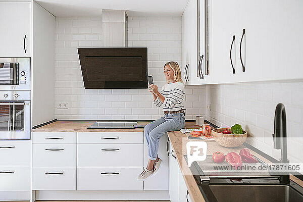 Frau benutzt Mobiltelefon in heimischer Küche zu Hause