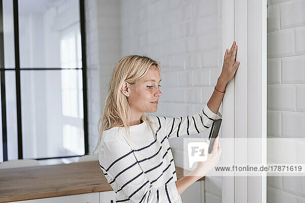 Young woman with smart phone touching radiator at home