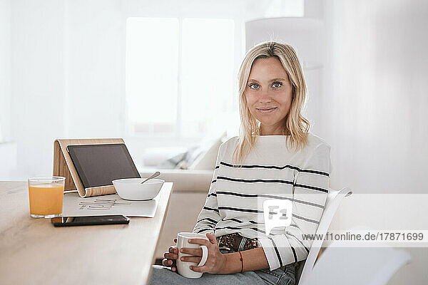Smiling woman with coffee cup and tablet PC on table at home