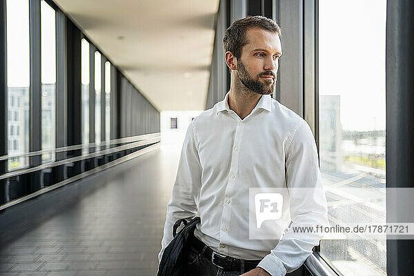 Contemplative young businessman looking through window at elevated walkway