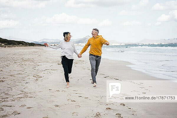 Happy mature couple holding hands and running at beach