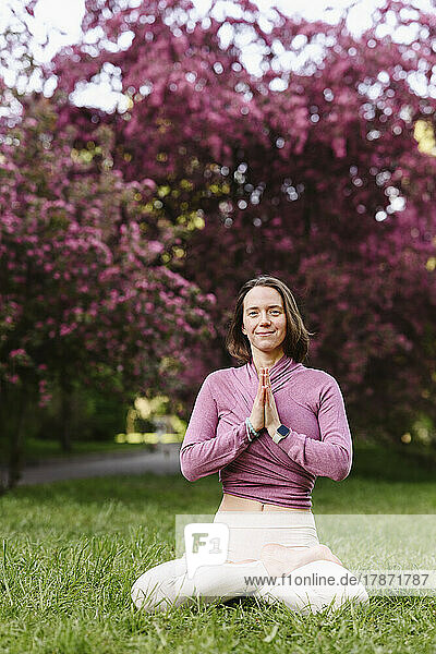 Smiling woman with hands clasped doing yoga sitting in apple blossom garden