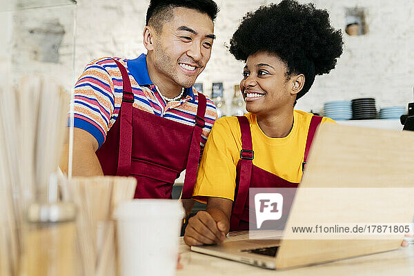 Smiling young man and woman sharing laptop in cafe