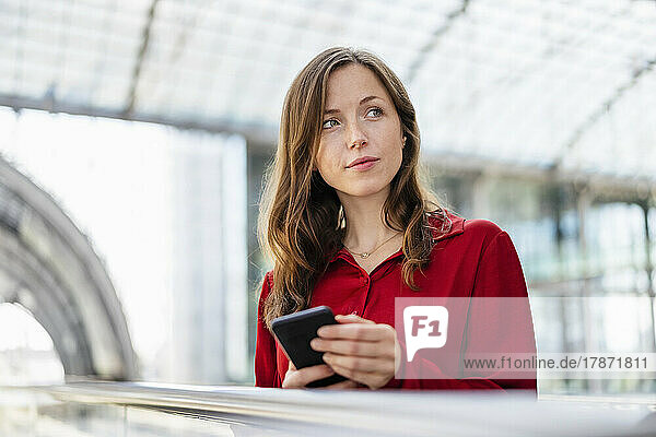 Contemplative woman with brown hair holding smart phone