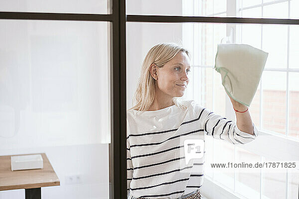 Smiling woman cleaning glass wall at home
