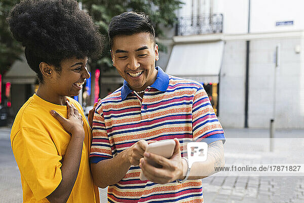 Cheerful young woman looking at man using smart phone