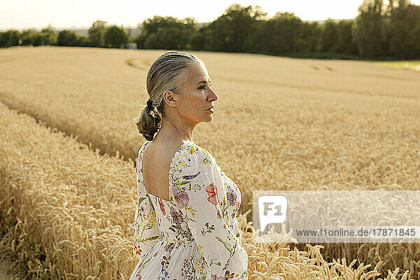 Senior woman wearing summer dress standing in wheat field