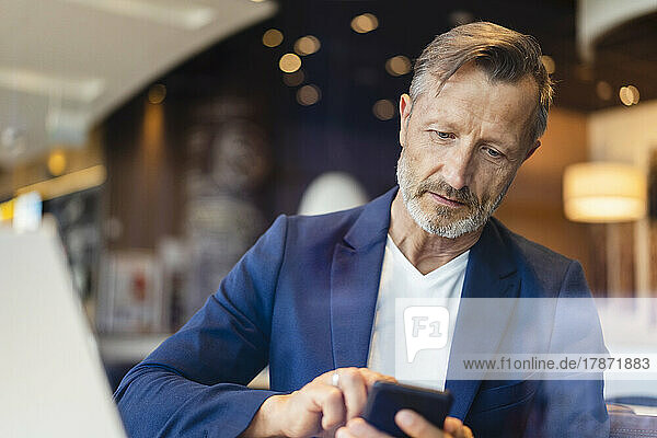 Mature businessman in blazer using smart phone at cafe