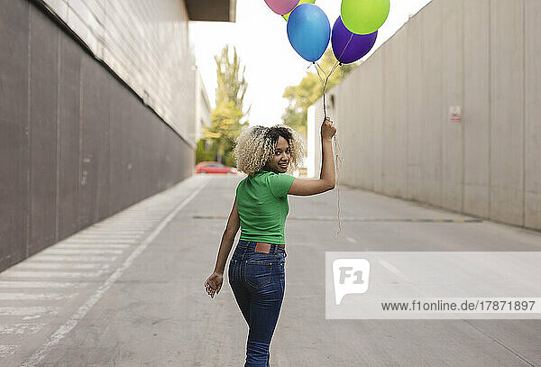 Smiling woman with multi colored balloon walking on road