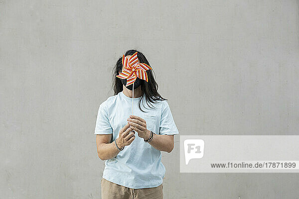 Man covering face with pinwheel toy in front of wall
