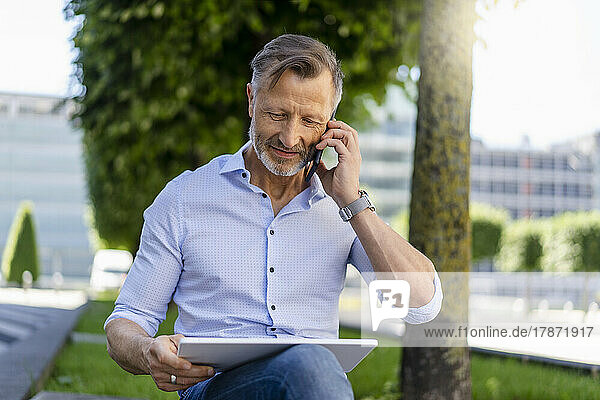 Businessman talking on smart phone using digital tablet at office park