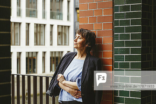 Contemplating woman with blazer leaning on wall