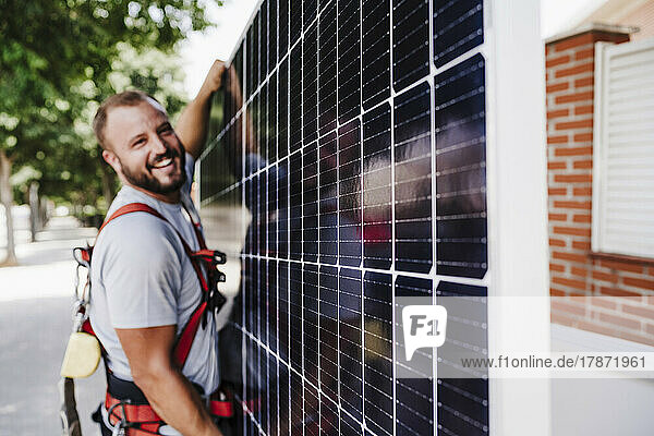 Smiling technician carrying heavy solar panel