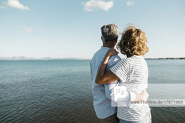 Älteres Paar mit umarmten Armen und Blick aufs Meer an einem sonnigen Tag