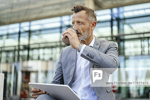 Businessman drinking coffee holding digital tablet in front of building