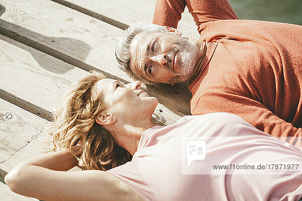 Smiling mature couple lying on jetty floorboard