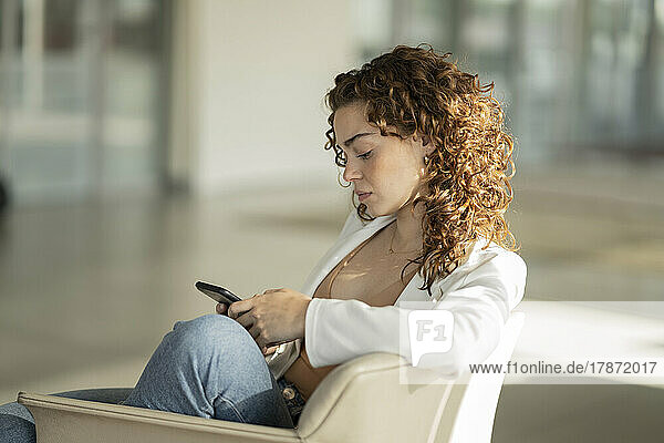 Young businesswoman with brown curly hair using mobile phone in office