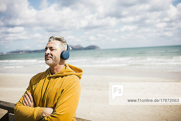 Smiling man with eyes closed listening music through wireless headphones