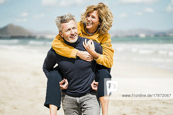 Happy man giving piggyback ride to woman at beach on sunny day