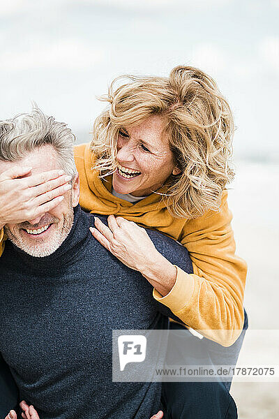Glückliche Frau bedeckt die Augen eines Mannes mit der Hand am Strand
