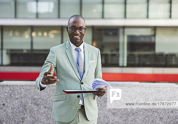 Happy businessman with documents gesturing in front of building