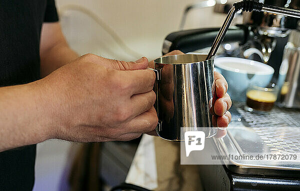 Hand of man holding mug making coffee in cafe