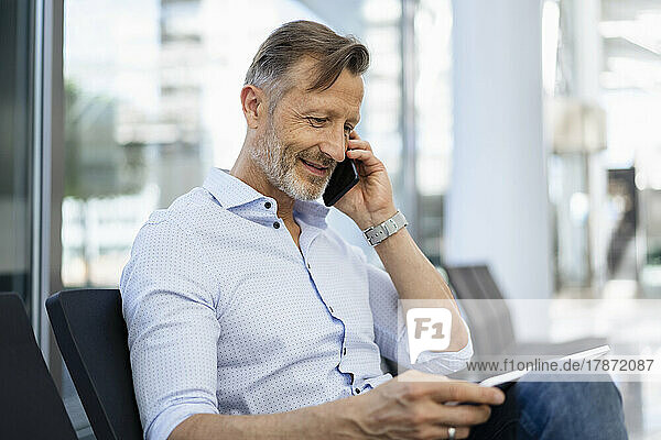 Lächelnder Geschäftsmann  der mit einem Grafiktablett auf dem Smartphone spricht