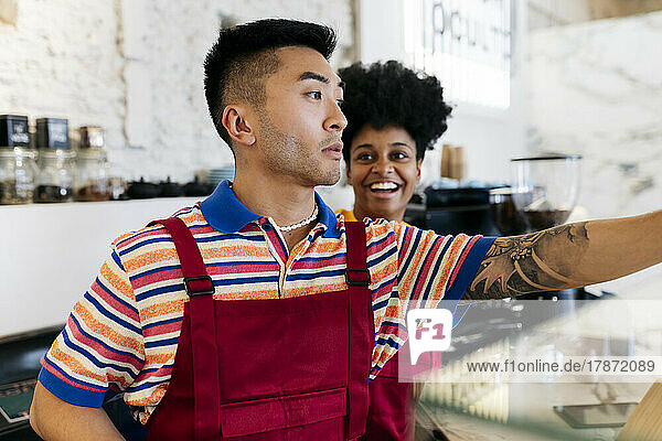 Happy young man looking at colleague working in coffee shop